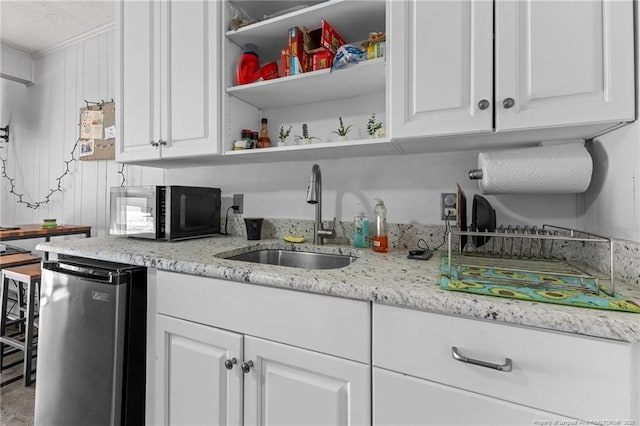 kitchen with dishwashing machine, a sink, white cabinets, light stone countertops, and open shelves