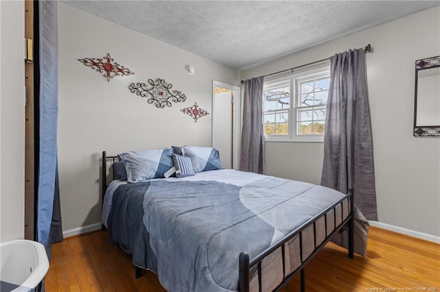 bedroom featuring a textured ceiling, baseboards, and wood finished floors