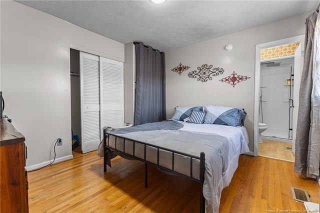 bedroom featuring a closet, visible vents, light wood finished floors, and ensuite bathroom