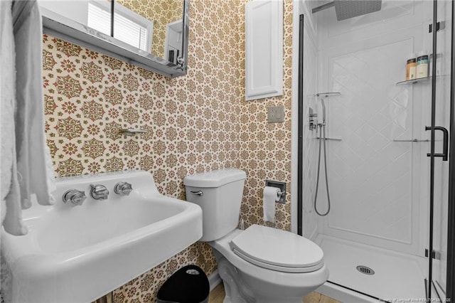 bathroom with a stall shower, a sink, toilet, and wallpapered walls