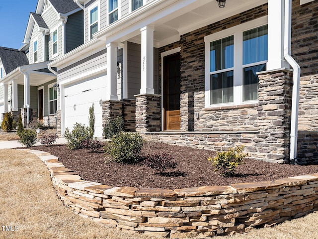 doorway to property featuring stone siding, covered porch, and an attached garage