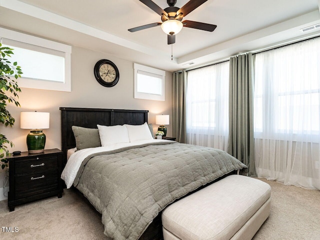 bedroom featuring light carpet, a ceiling fan, visible vents, and a tray ceiling