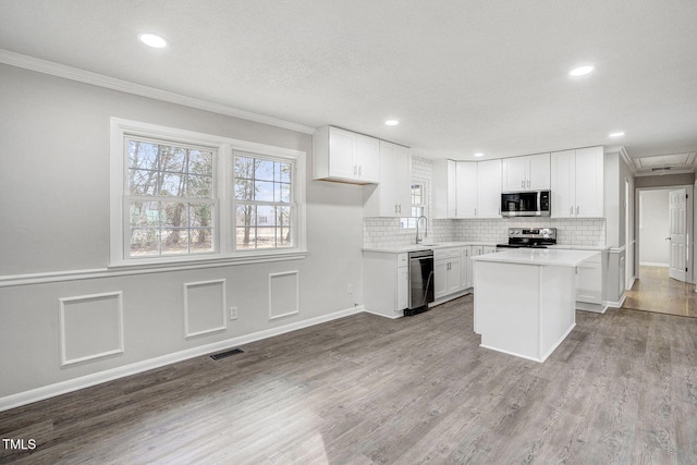 kitchen with visible vents, a kitchen island, appliances with stainless steel finishes, light countertops, and white cabinetry