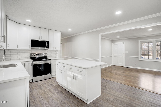 kitchen with stainless steel appliances, a sink, white cabinets, light wood-type flooring, and a center island