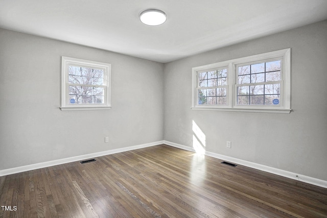 spare room featuring dark wood-style floors, visible vents, and baseboards