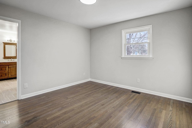 unfurnished room featuring dark wood-type flooring, visible vents, and baseboards