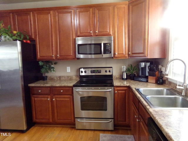 kitchen featuring brown cabinetry, stainless steel appliances, light countertops, light wood-style floors, and a sink