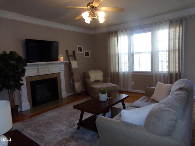 living room featuring crown molding, a high end fireplace, ceiling fan, wood finished floors, and baseboards