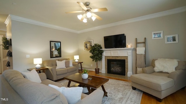 living room with a ceiling fan, crown molding, a fireplace with flush hearth, and wood finished floors