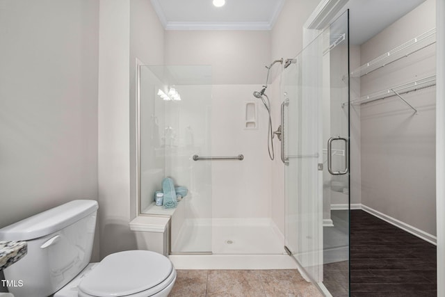 bathroom with toilet, baseboards, a spacious closet, a stall shower, and crown molding