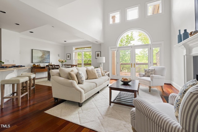 living room featuring crown molding, wood-type flooring, baseboards, and a towering ceiling