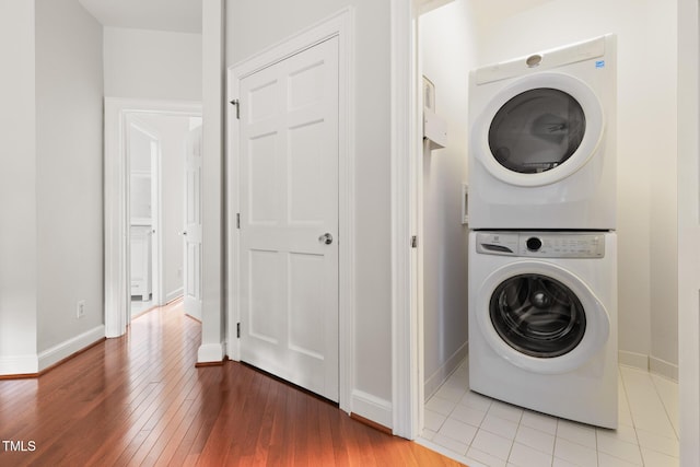laundry room featuring laundry area, stacked washer and clothes dryer, baseboards, and light wood-type flooring