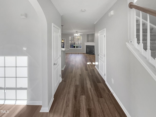 hall featuring arched walkways, dark wood-type flooring, baseboards, stairway, and crown molding