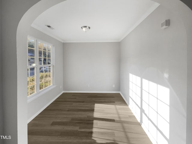 empty room featuring arched walkways, crown molding, visible vents, wood finished floors, and baseboards