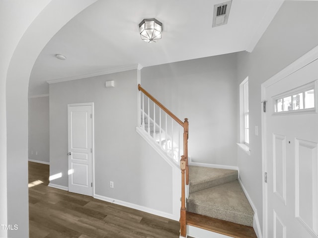 staircase with arched walkways, visible vents, ornamental molding, wood finished floors, and baseboards