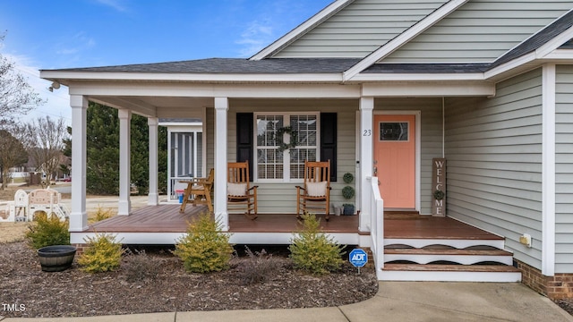 view of exterior entry featuring covered porch and a shingled roof