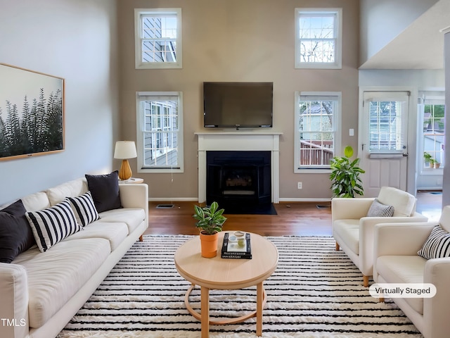 living room featuring dark wood-style floors, a fireplace with flush hearth, a towering ceiling, and baseboards