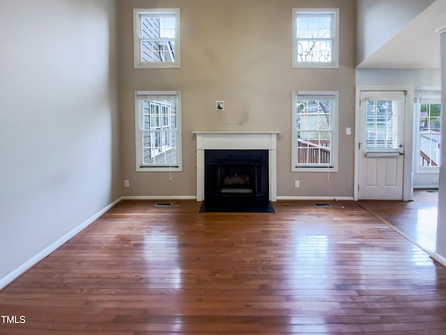 unfurnished living room with dark wood-style flooring, a fireplace with flush hearth, a towering ceiling, and baseboards