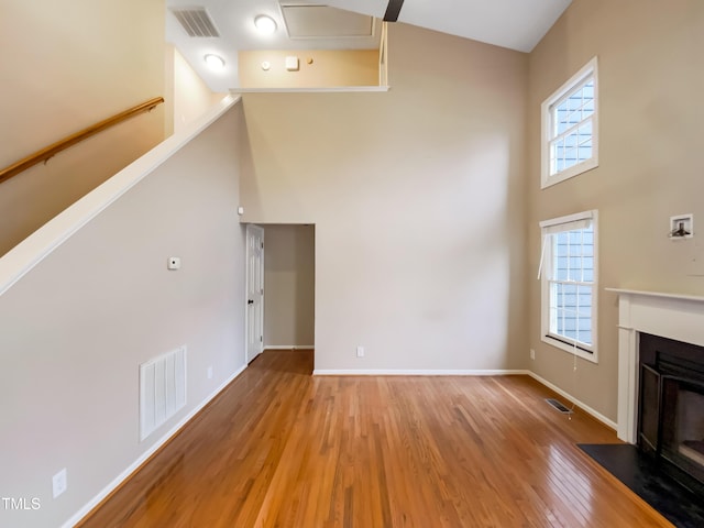 unfurnished living room with a fireplace with flush hearth, light wood-type flooring, visible vents, and a high ceiling