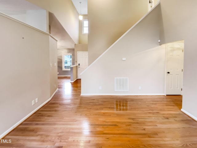 unfurnished living room featuring a high ceiling, wood finished floors, visible vents, and baseboards