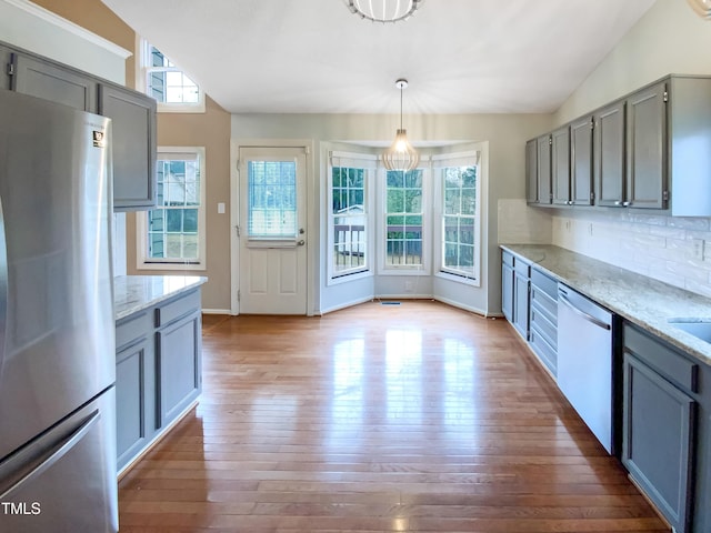 kitchen with lofted ceiling, hanging light fixtures, appliances with stainless steel finishes, and light stone counters