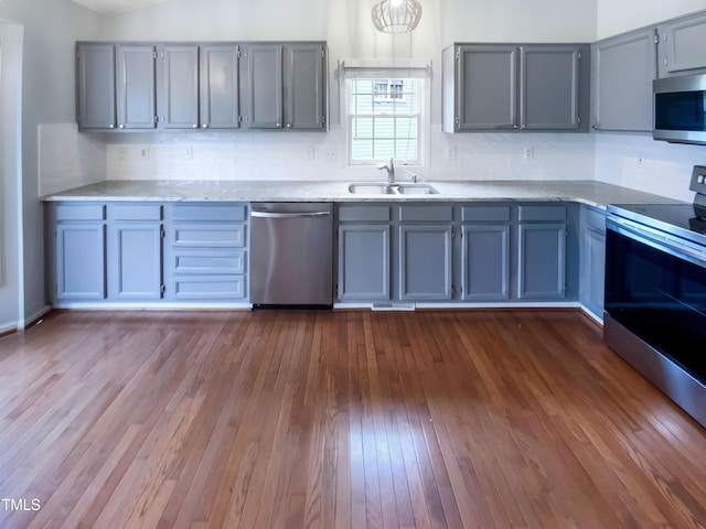 kitchen with dark wood-style flooring, stainless steel appliances, light countertops, gray cabinetry, and a sink