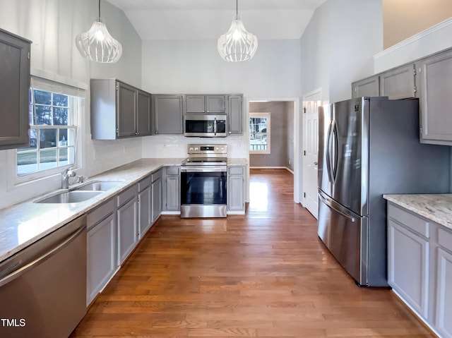 kitchen featuring high vaulted ceiling, appliances with stainless steel finishes, a sink, and decorative light fixtures