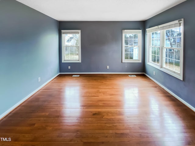 empty room featuring dark wood-style floors, visible vents, and baseboards