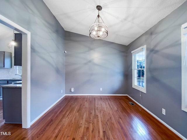 spare room featuring a notable chandelier, hardwood / wood-style floors, visible vents, and baseboards