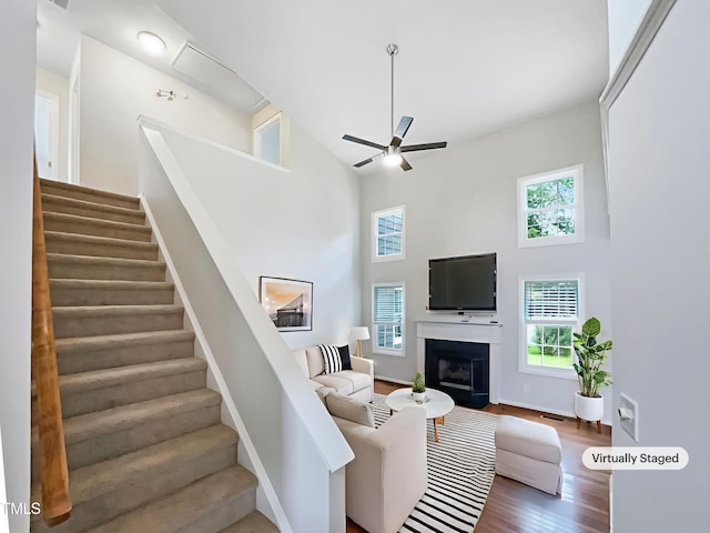 5317 Tifton Dr, Raleigh, NC 27610 - living room featuring a high ceiling, ceiling fan, stairs, wood finished floors, and a fireplace with flush hearth