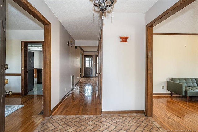 corridor with brick floor, visible vents, a textured ceiling, and baseboards