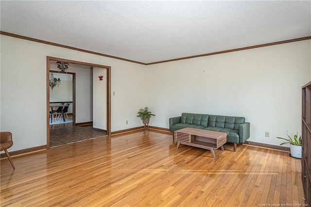 living room featuring a textured ceiling, ornamental molding, light wood-style flooring, and baseboards