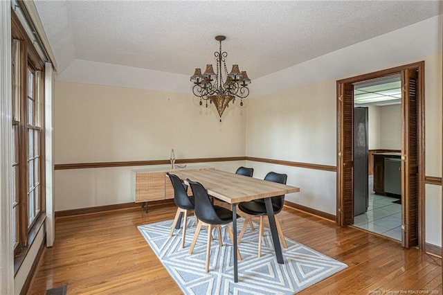 dining room featuring light wood-type flooring, visible vents, a textured ceiling, and an inviting chandelier