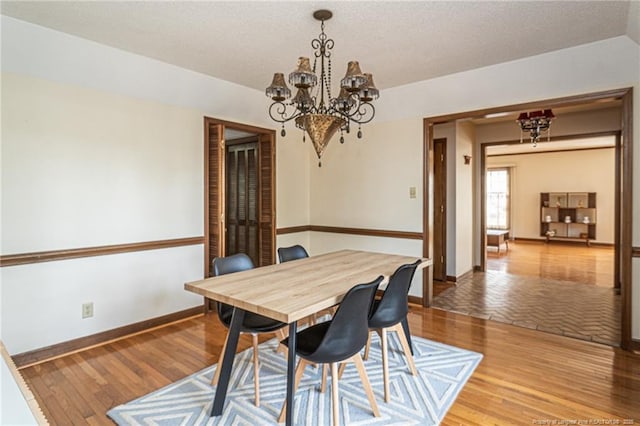 dining room featuring an inviting chandelier, a textured ceiling, baseboards, and wood finished floors