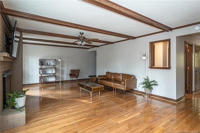 living room with light wood finished floors, baseboards, a textured ceiling, a fireplace, and beam ceiling