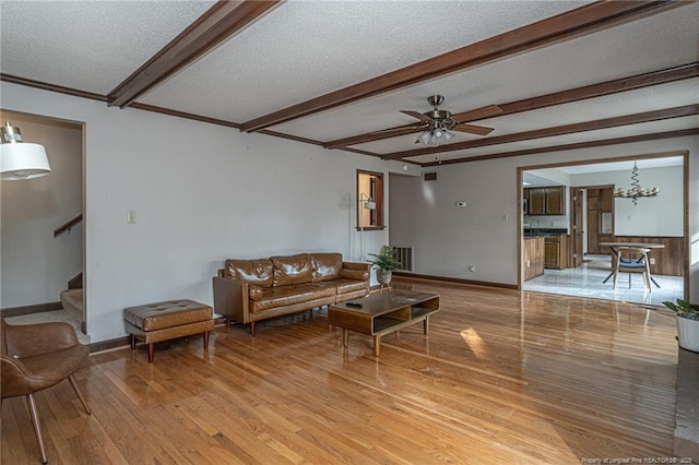 living area with wood finished floors, beamed ceiling, a textured ceiling, and stairs