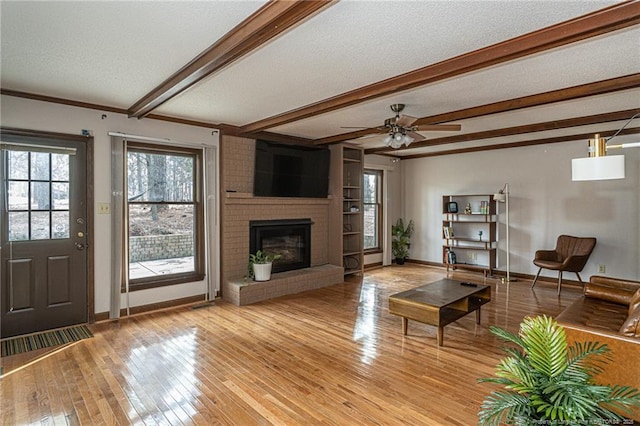 living area featuring a textured ceiling, light wood-style flooring, a fireplace, baseboards, and beamed ceiling