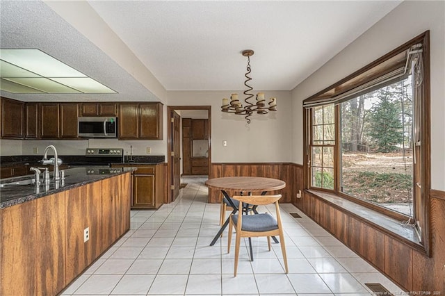 kitchen with a wainscoted wall, appliances with stainless steel finishes, decorative light fixtures, a sink, and light tile patterned flooring