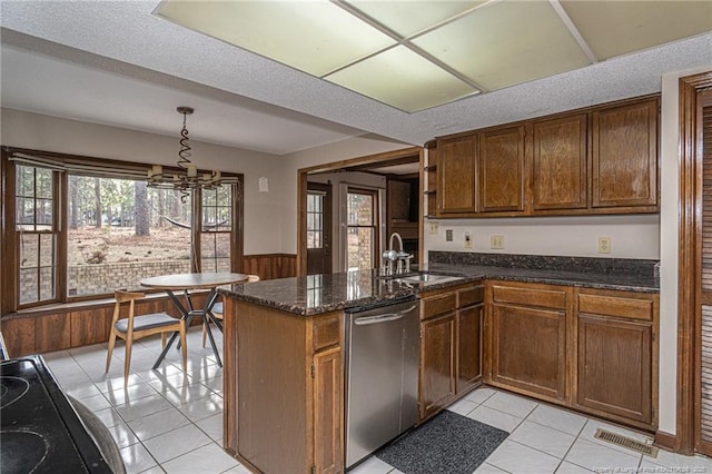 kitchen featuring wainscoting, decorative light fixtures, a peninsula, stainless steel dishwasher, and a sink