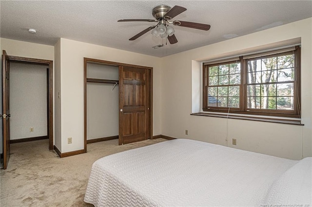 bedroom with a closet, light colored carpet, a textured ceiling, and baseboards