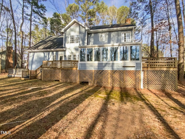 rear view of property with a sunroom, a chimney, a deck, and a yard