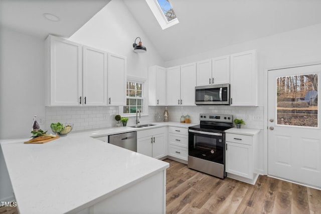 kitchen with a skylight, appliances with stainless steel finishes, a peninsula, light countertops, and a sink