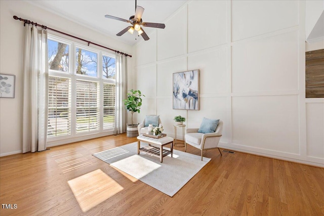 living area featuring visible vents, a ceiling fan, a towering ceiling, light wood-type flooring, and a decorative wall