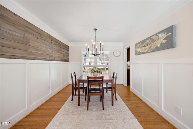 dining room with a chandelier, ornamental molding, wood finished floors, and a decorative wall