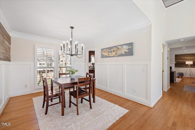 dining area with a wainscoted wall, ornamental molding, an inviting chandelier, light wood-style floors, and a decorative wall