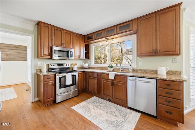 kitchen with appliances with stainless steel finishes, brown cabinetry, a sink, and light wood finished floors