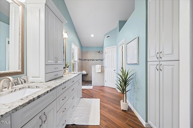 bathroom with double vanity, baseboards, wood finished floors, walk in shower, and a sink