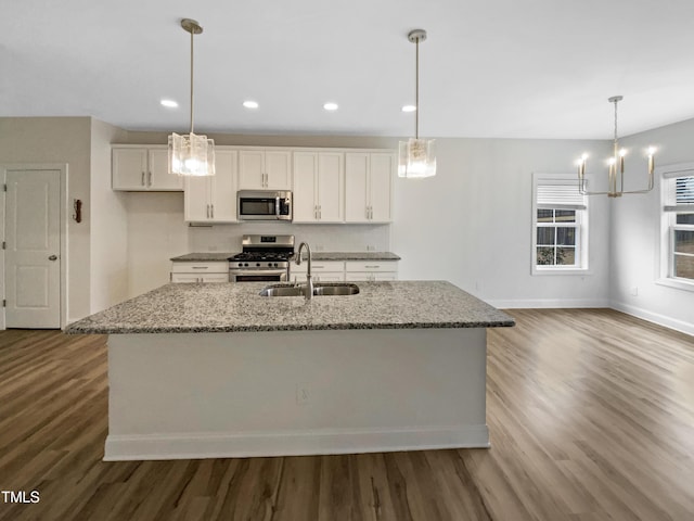 kitchen featuring a center island with sink, light stone counters, decorative light fixtures, stainless steel appliances, and a sink