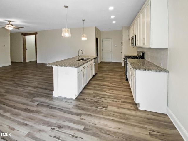 kitchen with dark stone counters, decorative light fixtures, stainless steel appliances, white cabinetry, and a sink