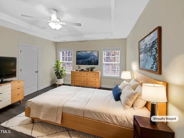 bedroom featuring ceiling fan, dark colored carpet, a tray ceiling, and baseboards